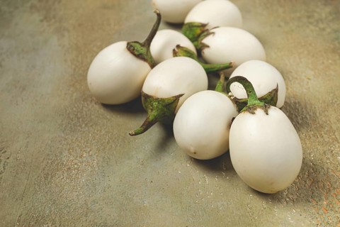 Several white eggplants are placed on a textured surface. The scene is well-lit and emphasizes the