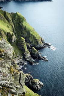 Green, rugged cliffs fall steeply into the blue sea, slightly cloudy sky, bird protection island,
