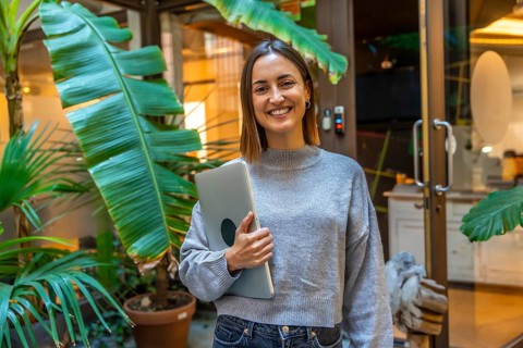 Portrait of a smiling young woman outside a coworking space holding a laptop