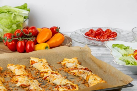 Baked pizza sticks on a tray, next to ingredients and fresh salad, pizza