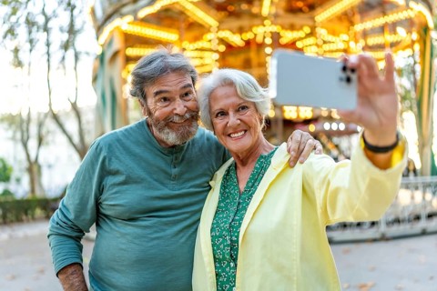 Caucasian senior couple smiling at camera while talking selfie in a city fair
