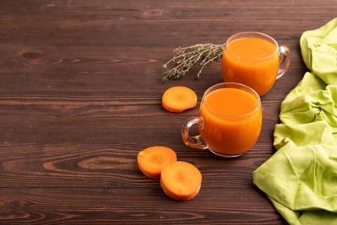 Two glasses with carrot juice, on wooden background and green textile. Diet, healthy eating concept