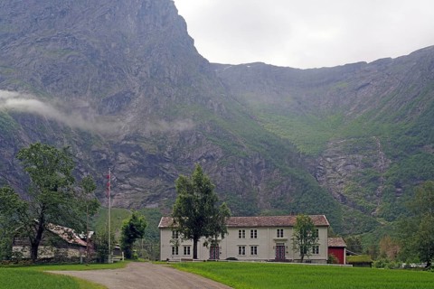 White house in a valley between high mountains with cloudy sky, Raumadalen, Trollvegen, Andalsnes,