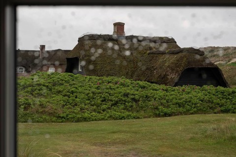 View through a window with blurred raindrops, traditional thatched Danish houses in the background,