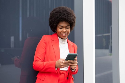 A confident woman in a bright red suit using a smartphone while standing outside by a reflective