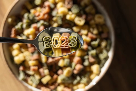 A spoonful of numerically shaped pasta displays the year 2026 above a bowl full of colorful number