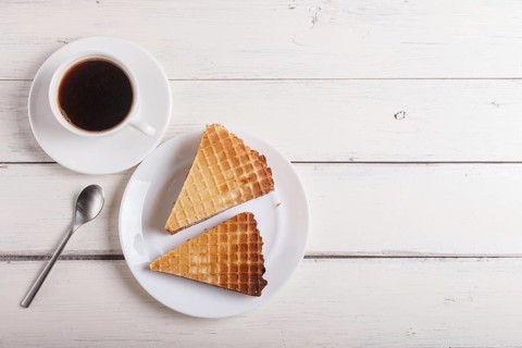 Waffle sandwiches with boiled condensed milk in plate on white wooden table with cup of coffee.