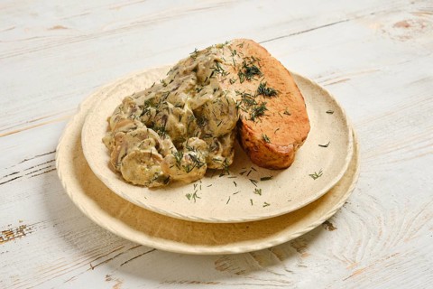 Creamy sauce with mushrooms covers slices of roasted pork meat. A sprinkle of herbs decorates the