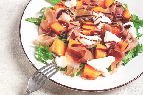 Salad with slices of ripe melon, prosciutto, mozzarella and fresh arugula, decorated with balsamic