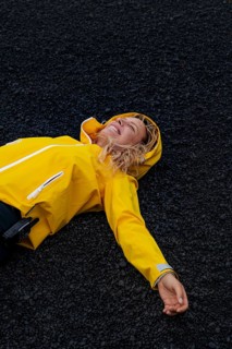 A woman in a yellow jacket enjoys a blissful moment lying on the black volcanic terrain of