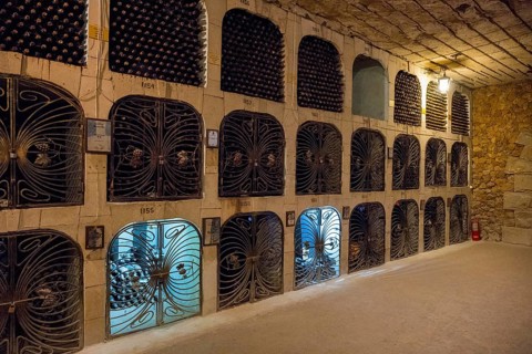 Wine cellar with well-lit bottle racks, which are partially secured by metal mesh doors, wine