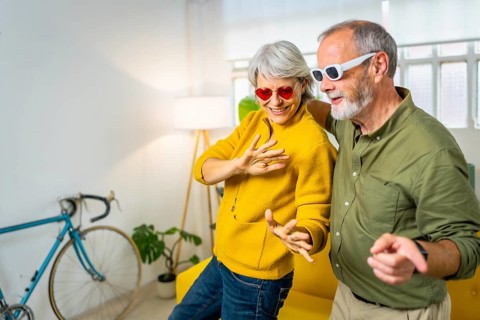 Happy modern senior couple with sunglasses dancing and having fun at home