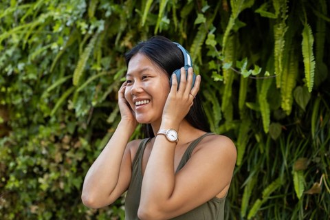 A cheerful Chinese woman wears headphones and enjoys music outdoors. Surrounded by lush greenery,