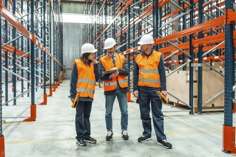 Warehouse workers and manager discussing logistics using a digital tablet, surrounded by shelves in