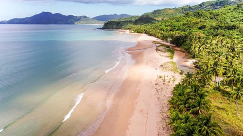 A scenic aerial photograph featuring a remote beach surrounded by lush greenery and mountains,