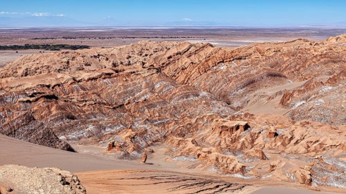Sandy, steep rock formations in a vast desert landscape under blue skies, The Moon Valley in the