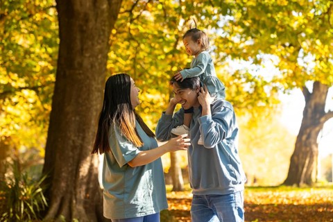 An Asian family enjoys a sunny day at the park, with a mother and father smiling while their young