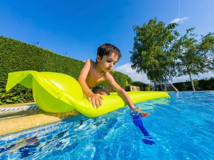 Young child enjoying a sunny summer day, dipping a water gun into the blue water from a brightly
