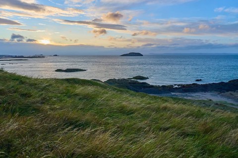 View of sea and island at sunset, with grassy hills in the foreground, North Berwick, East Lothian,