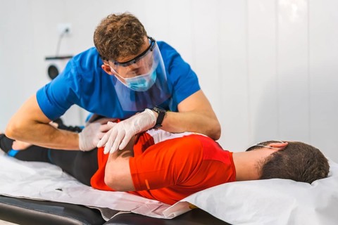 A physical therapist working on the hip of a patient. Physiotherapy with protective measures for