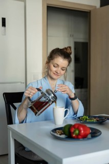 A woman in a casual setting pours tea into a mug at her kitchen table, creating a warm and cozy