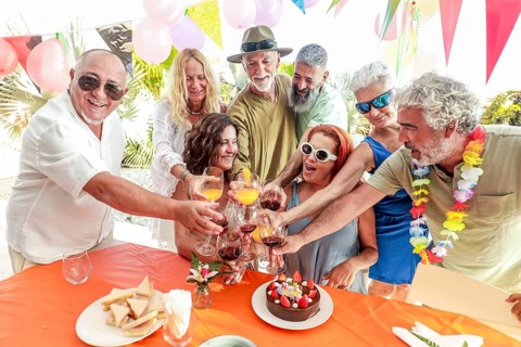 A group of friends happily toasting with drinks at an outdoor birthday party, surrounded by