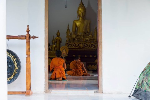 Laotian novices in orange robes in front of a golden Buddha figure in a newly built Buddhist