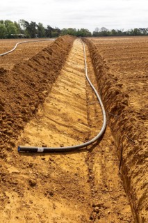 Poly pipe subsurface irrigation system in excavated ditch across sandy field, Shottosham, Suffolk,