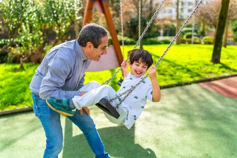 Grandfather and grandson enjoying a sunny day at the playground, pushing the swing and having fun