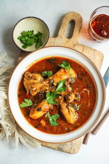 A savory chicken stew served in a round white dish, garnished with fresh coriander. The rich, red