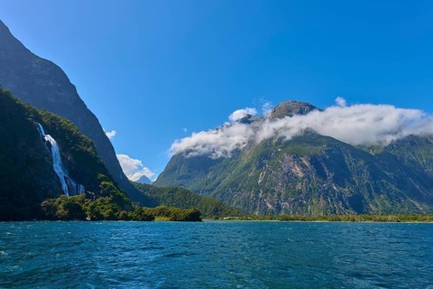 Blue fjord with waterfall in the background and impressive mountains under a blue sky, summer,