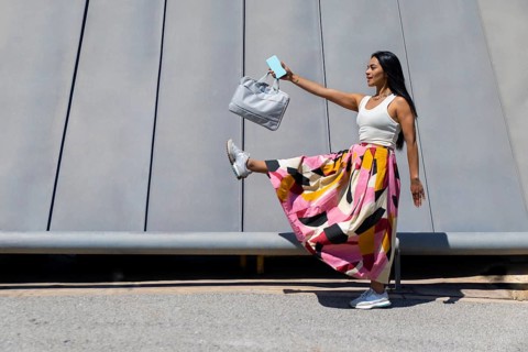 A stylish woman in a vibrant outfit contrasts against modern architecture. Captured mid-motion, she
