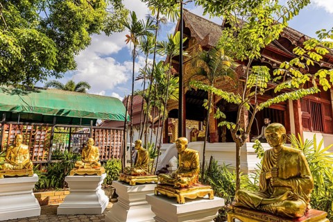 Gilded monk statues sitting on pedestal in the garden of the Wat Phra Singh Buddhist temple
