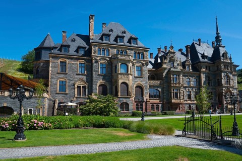 An imposing castle with historic architecture stands in a well-tended park under a blue sky, Lieser