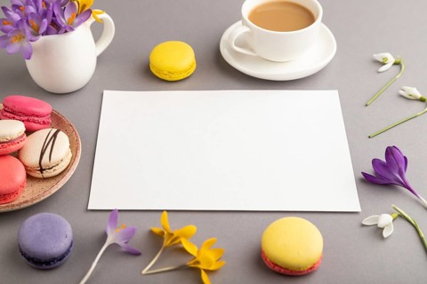 White paper sheet mockup with spring snowdrop crocus flowers and multicolored macaroons on gray