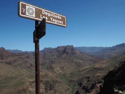 Signpost in the foreground in a dry mountain landscape with clear blue sky, Barranco de Fataga,