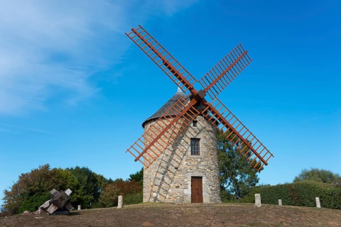 Stone windmill with large wooden sails on a sunny day on a hill, Buglais mill, Lancieux,