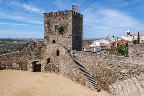 Castle complex with tower, stairs and view of a historic city under clear skies, Monsaraz, Évora,