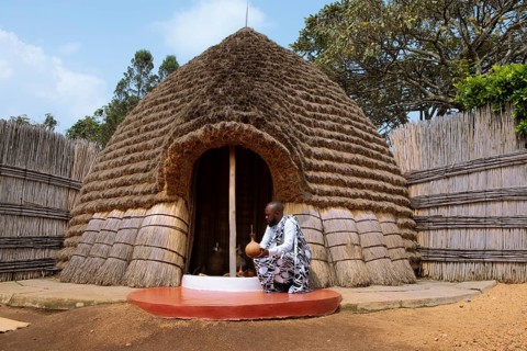 Rwandan man, 25 years old, wearing traditional clothing at the entrance to the beehive shaped beer