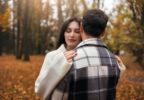 A couple embraces in an autumn forest surrounded by vibrant leaves. The woman closes her eyes with