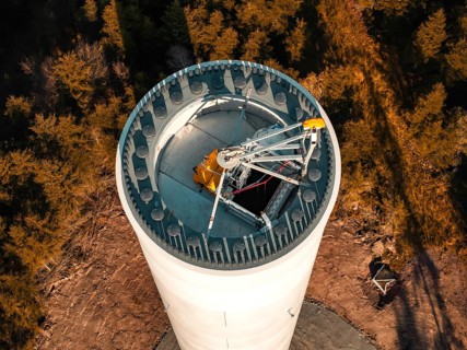 A wind turbine in a wooded area seen from above, surrounded by autumnal trees, wind turbine