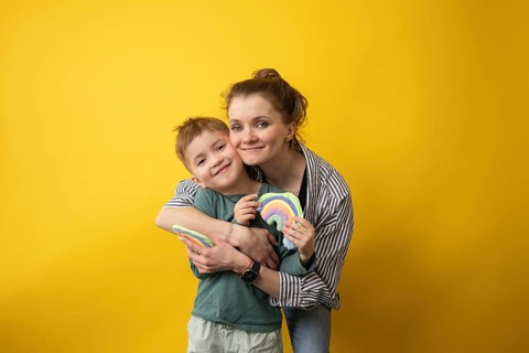 A joyful teacher hugs her smiling student as they proudly display rainbow crafts. The warm,