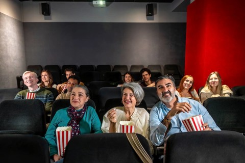 People of different ages and ethnicities are watching a film and eating popcorn in a movie theater,