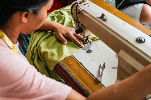 A asian seamstress skillfully sewing green fabric using a sewing machine. The workspace is equipped
