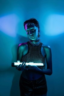 A futuristic cyberpunk woman stands confidently holding a glowing neon light against a vibrant blue