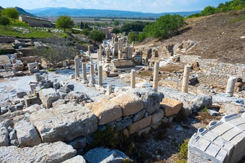 Ancient ruins with columnar trails surrounded by green nature and mountains in the background,