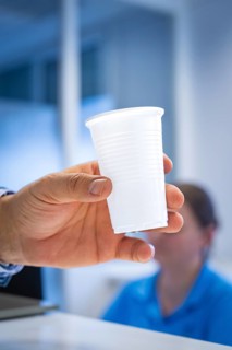 A hand holding a plastic cup at a reception counter with blurred background, Urology, Germany