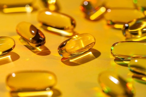 Softgel capsules scattered on a vibrant yellow surface, filled with essential vitamins. Perfect as