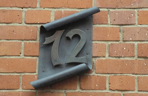 Black house sign 12 on rolled metal sheet, number, number, rolled, handmade, ironwork, red bricks,