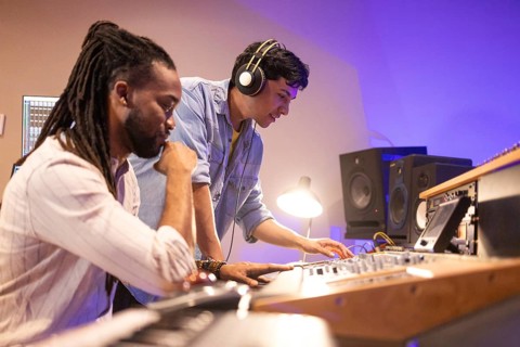 Two musicians collaborate in a state-of-the-art recording studio. One wears headphones, operating a